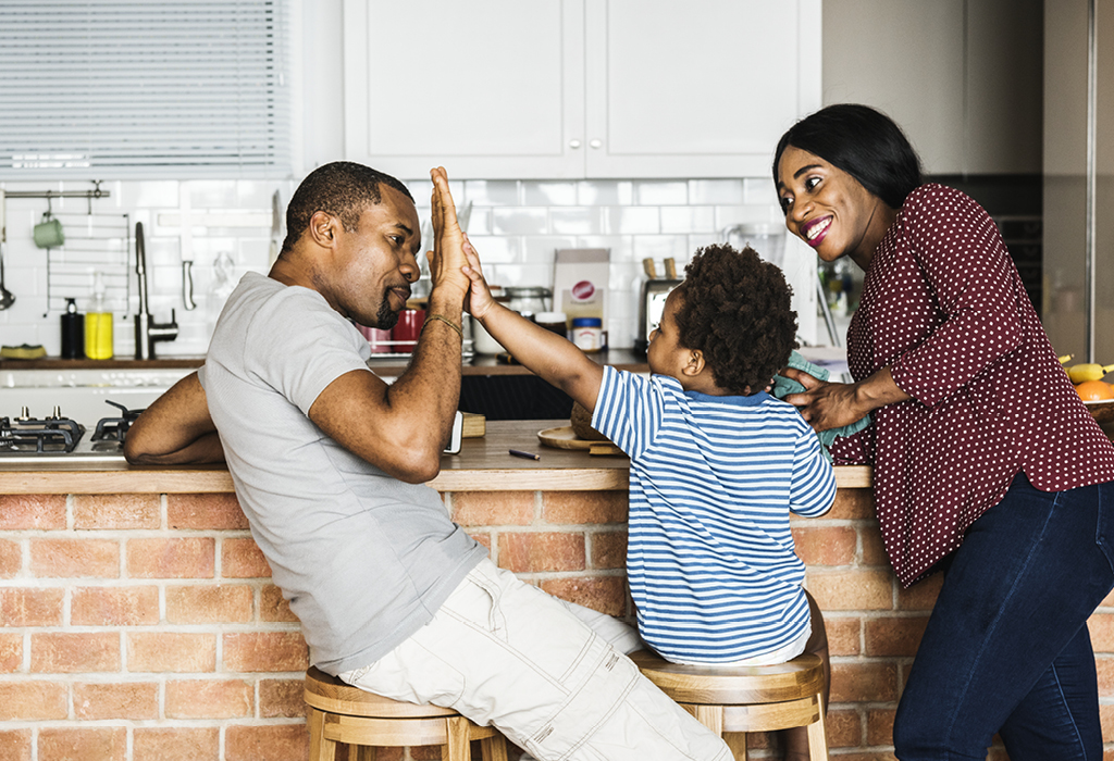 Dad high-fiving son while sitting in-front of the kitchen counter.